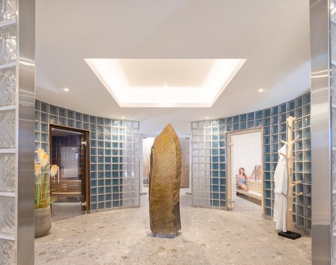 Eleganter Wellnessbereich mit zentralem Naturstein, Glaswänden und Zugängen zu verschiedenen Saunen.