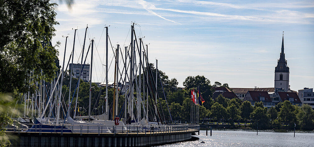 Segelboote im Hafen von Friedrichshafen am Bodensee mit der Schlosskirche im Hintergrund an einem sonnigen Tag.