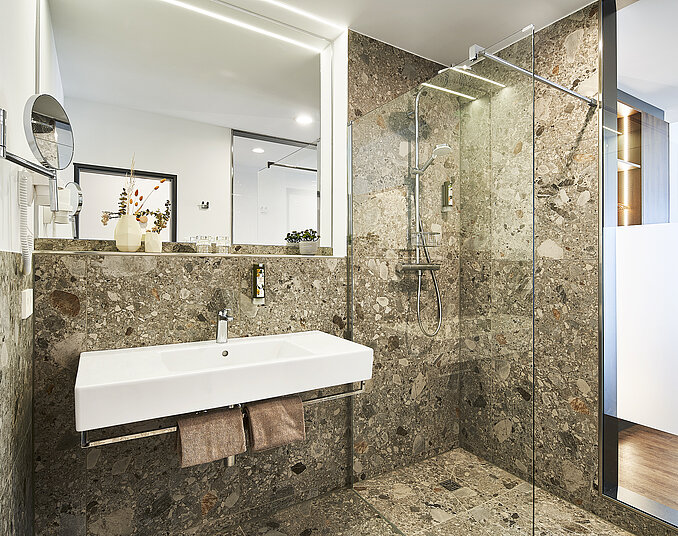 Modernes Badezimmer mit Natursteinfliesen, großer begehbarer Dusche und stilvollem Waschbecken.