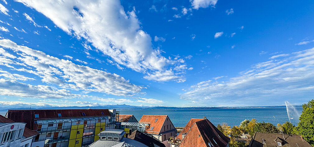 Panoramablick über Friedrichshafen mit malerischem Bodensee und Alpenkulisse unter einem strahlend blauen Himmel.