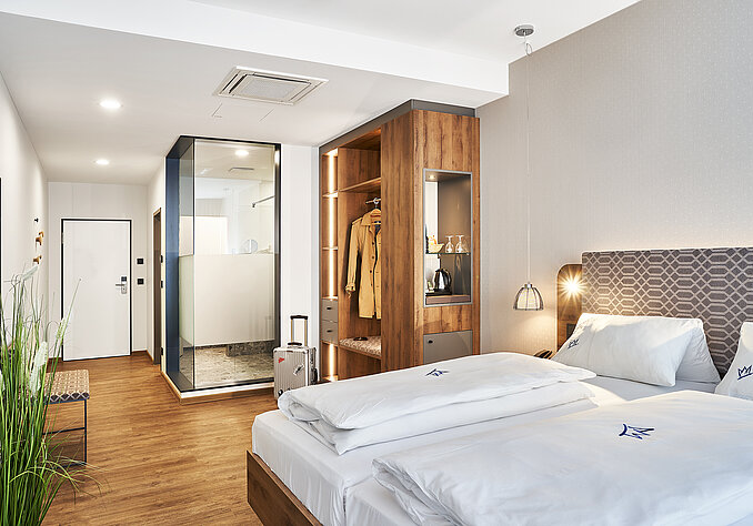 Modernes Hotelzimmer mit gemütlichem Doppelbett, offenem Kleiderschrank und verglastem Badezimmer.