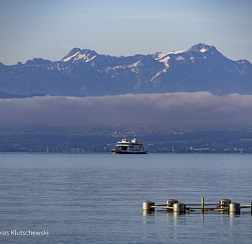 Fähre auf dem Bodensee mit Blick auf die schneebedeckten Alpen im Hintergrund an einem klaren Morgen.