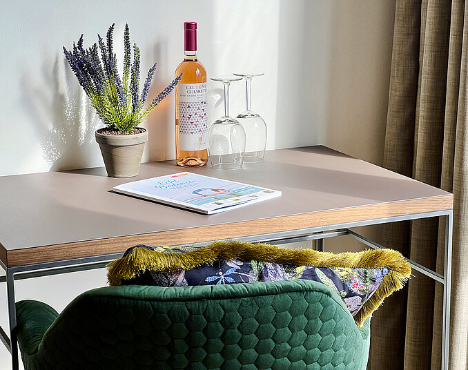 Stilvoll eingerichteter Schreibtisch mit Roséwein, Weingläsern, Lavendelpflanze und einer Broschüre.