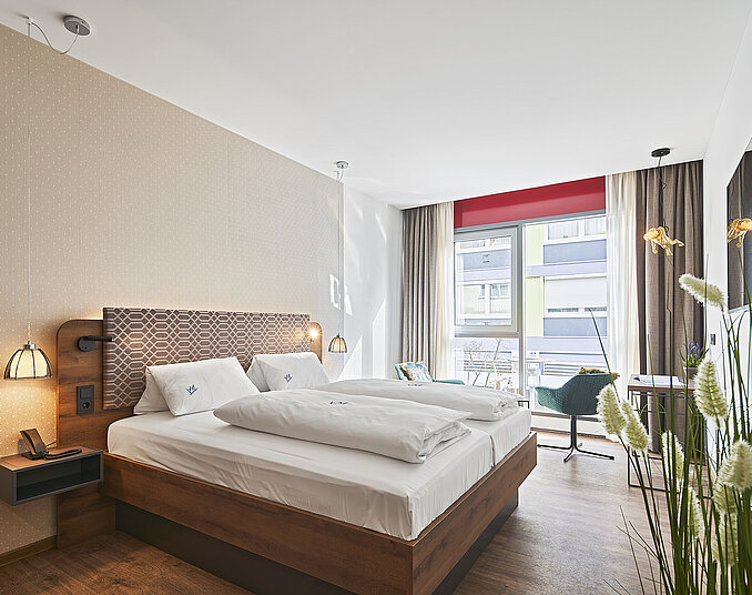 Helles Hotelzimmer mit gemütlichem Doppelbett, stilvoller Einrichtung und bodentiefem Fenster mit Stadtblick.