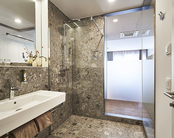 Modernes Badezimmer mit Natursteinfliesen, begehbarer Regendusche, stilvollem Waschbecken und großen Spiegeln.