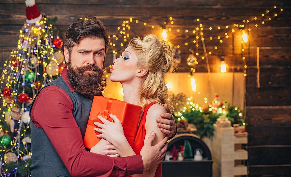Pärchen im Weihnachtsoutfit und ein Weihnachtsbaum im Hintergrund.