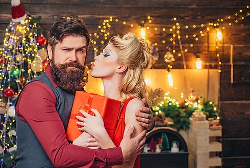 Pärchen im Weihnachtsoutfit und ein Weihnachtsbaum im Hintergrund.