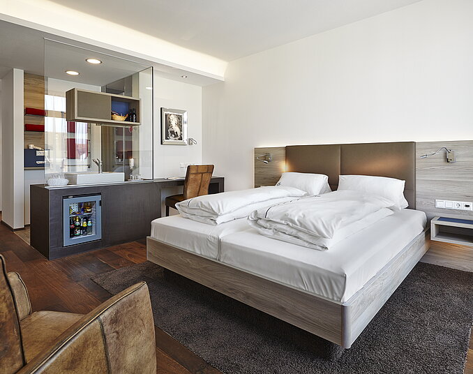 Modernes Hotelzimmer mit großem Doppelbett, offenem Badezimmer, Schreibtisch und stilvollem Design.
