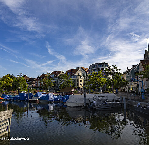 Kleine Boote im Hafen von Friedrichshafen vor malerischer Altstadtkulisse bei blauem Himmel.
