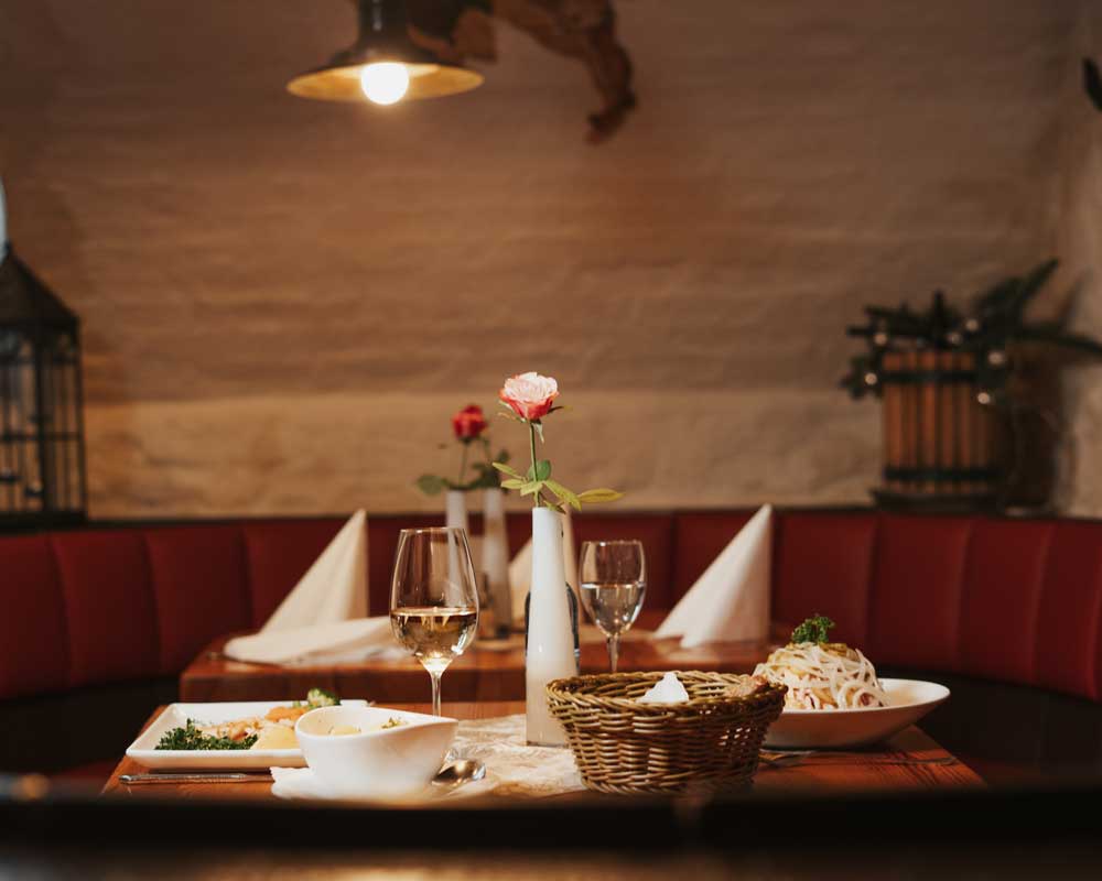 Gemütlich gedeckter Tisch mit Pasta und Wein in einem stimmungsvollen Restaurantambiente.