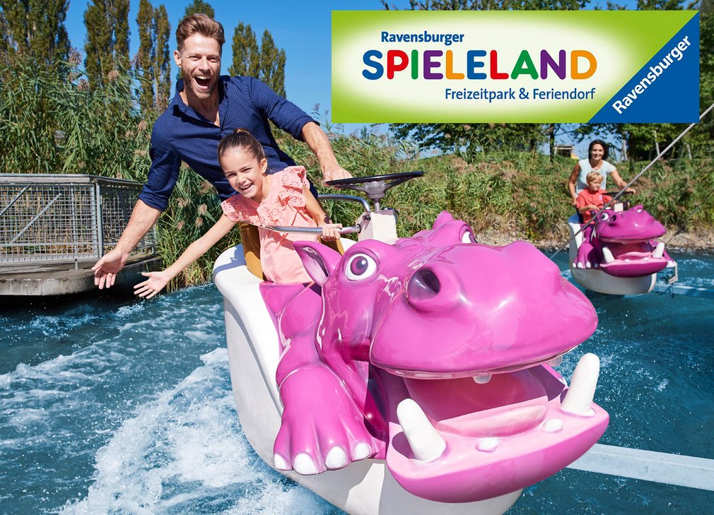 Eine lächelnde Frau und ein Kind fahren auf einem pinken Wasserfahrzeug in Form eines Nilpferds durch einen Freizeitpark. Im Hintergrund ist ein weiteres Fahrzeug zu sehen. Oben links befindet sich das Logo des Ravensburger Spielalands.